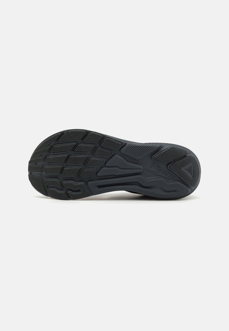 Suela de zapato de goma negra con un patrón texturizado que presenta surcos y aristas para mejorar la tracción. La forma es redondeada con un tacón ligeramente elevado.