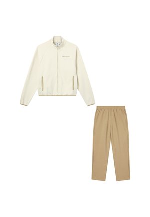 Chaqueta cremosa con cremallera y mangas raglán, con bolsillos laterales, combinada con pantalones elásticos en color marrón claro, ambos de tejido suave.