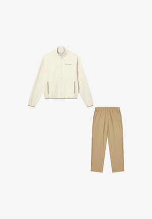 Lichtbeige ritsjack met raglanmouwen en zijzakken, gecombineerd met bijpassende tan elastische taillebroek, beide gemaakt van zacht materiaal.