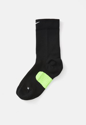 Schwarze Sportsocke mit strukturiertem Oberflächen, ausgestattet mit einem leuchtend grünen Akzent an der Ferse und einem weißen Logo nahe dem Bündchen.