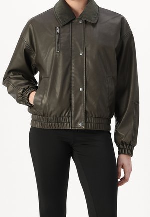 Ciemnozielona kurtka typu bomber z ekoskóry z żebrowanym kołnierzem, elastycznymi mankietami i pasem, przednim zapięciem na zatrzaski, zamykaną kieszenią na piersi, noszona z czarnymi spodniami.