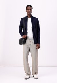 Navy zip-up cardigan over a white t-shirt, light blue jeans, and black crossbody bag. White and black sneakers complete the outfit.