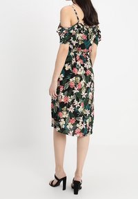 Černé květinové šaty s krátkými rukávy, zdobené růžovými a bílými květy. Šaty mají přiléhavý pas a délku po kolena. Nošeny s černými lodičkami.