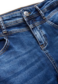 Siniset farkut, joissa on kevyt kuluma, hopeinen nappi, oranssit tikkausviivat ja viisi taskua. Sujuva pinta, rento tyyli.