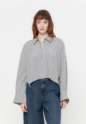 Black and white striped collared shirt with wide sleeves, cropped hem, and button closure, paired with loose blue denim jeans.