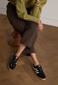 Black athletic shoes with a textured finish, featuring white stripes and a leopard-print accent on the heel. Cork outsole.