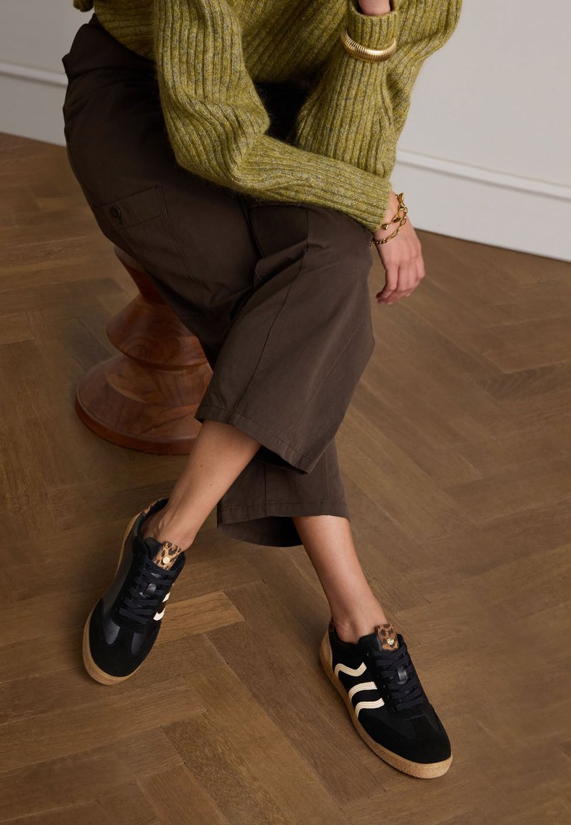 Black athletic shoes with a textured finish, featuring white stripes and a leopard-print accent on the heel. Cork outsole.