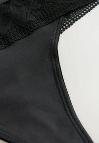 Lingerie noire avec une finition satinée lisse et un bord en dentelle florale. Présente des bords en dentelle délicats et une texture douce.