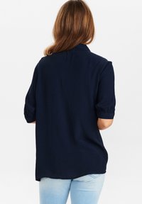 Camicia blu navy a maniche corte realizzata in tessuto morbido, con una vestibilità comoda, dotata di colletto a bottoni e maniche arricciate, con un orlo leggermente curvato.