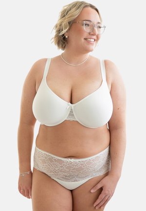 Smiling woman with glasses modeling white underwire bra and matching lace high-waist underwear, seen from front and looking right.