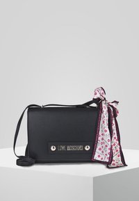 Borsa a tracolla nera in ecopelle con placca logo argentata, caratterizzata da una sciarpa a motivi rosa e bianca annodata al manico. Design piatto.