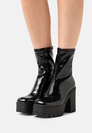 Svarta lackläder ankelboots med en snug passform, kraftig plattform och hög blockklack. Slät yta med sömnadsdetaljer.