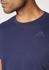 Navy zila kokvilnas T-krekls ar apaļu kaklu un mīkstu tekstūru, ar mazu izšuvumu kreisajā krūtī.