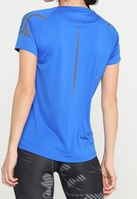 Modré atletické tričko s krátkými rukávy, s reflexními šedými prvky na ramenou a zádech, vyrobené z lehkého, hladkého materiálu.