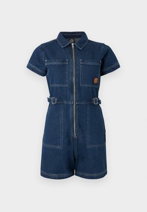 Tumesinine lühikeste varrukatega teksakangast kombinesoon ees oleva tõmblukuga, kahe rinnataskuga, reguleeritavate vöörihmadega ja vasakul rinnal väikese punase ja kollase plaastriga.