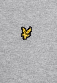 Tissu gris clair avec une texture douce, présentant un logo d'oiseau jaune brodé avec un contour noir sur le côté gauche.