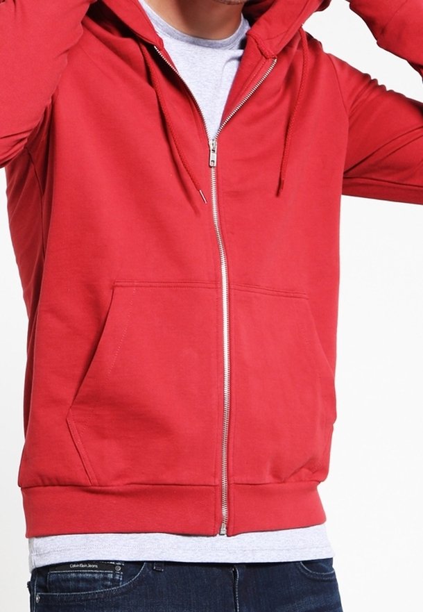 Sudadera roja con cremallera y un bolsillo frontal, hecha de una mezcla de algodón, con capucha y puños de canalé. Llevada sobre una camiseta gris.