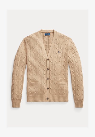 Bežs adīta džemperis ar V veida kaklu, priekšējām kabatām un pogām. Ribotas aproces un apakšmala ar mazu logotipu uz krūšu apgabala.