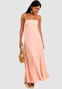 Rosa Maxikleid mit quadratischem Ausschnitt und dünnen Trägern, aus leichtem Stoff gefertigt. Es hat einen fließenden Rock und dezente Falten.