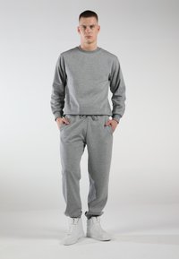 Gray sweatshirt and joggers made of soft fabric, featuring a classic crew neck, elastic waist, and side pockets. Worn with white sneakers.