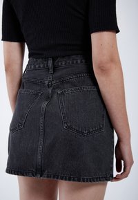 Zwarte denim minirok met een hoge taille, twee achterzakken en een rafelige zoom, met een gestructureerde stof en een klassieke snit.