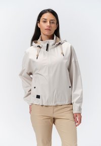 Lys beige jakke med hætte, frontlynlås og synlige snore. Har sidelommer og elastiske manchetter. Glat stoftekstur.