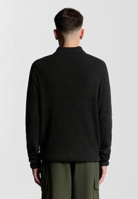 Ciemny dziergany sweter o prążkowanej fakturze, z kołnierzem i luźnym krojem, zestawiony z oliwkowozielonymi spodniami typu cargo.