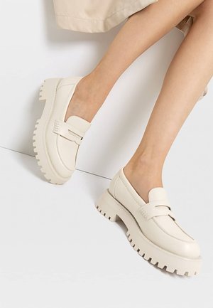 White leather loafers with a chunky, ribbed sole and side accents. Smooth texture, rounded toe shape, and slip-on design.