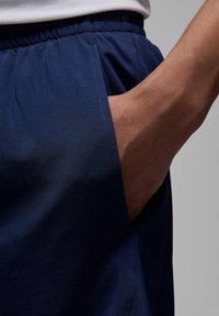 Marineblå shorts lavet af letvægtsstof med elastisk talje. Har en sidelomme og synlige stikninger langs kanten.