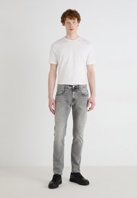 Könnyű, fehér pamut póló, ami slim fit szürke farmernadrággal és fekete sneaker-rel van párosítva. Egyenes szabás, kopottas hatású.