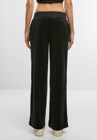 Schwarze Samt-Hosen mit weitem Bein und glatter Textur, die mit einem Logo-Muster versehen sind. Der Bund ist elastisch und sorgt für Komfort.