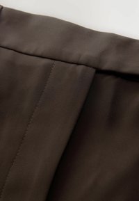 Tessuto marrone con una texture liscia, caratterizzato da una piega e dettagli di cucitura, adatto per abbigliamento o rivestimenti.