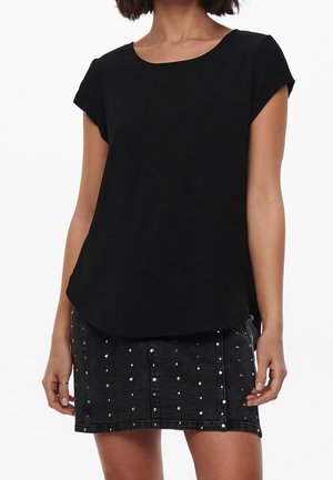 Femme portant un haut noir uni à manches courtes et une jupe en jean noire avec des clous argentés.