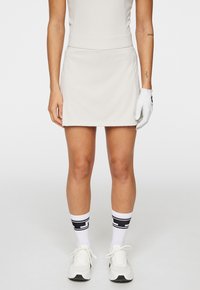 Ljusbeige idrottsmina med ett figursytt midjeband, ihop med vita strumpor med svarta ränder och vita sneakers. Handske på vänster hand.