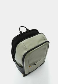 Zaino grigio e nero con un esterno liscio e imbottito, dotato di una tasca frontale con zip, maniglie doppie e una forma strutturata.