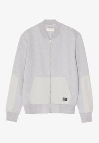 Sudadera gris con cremallera y cuello acanalado, parches en los codos en contraste beige y un gran bolsillo frontal. Presenta un logo en el bolsillo.