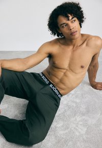 Calças de desporto verdes com uma cintura preta onde se lê "BJÖRN BORG" em letra branca; textura suave e corte descontraído.