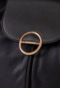 Black leather handbag with a rounded gold hardware ring closure. Textured finish on the leather, featuring a sleek design and detailed stitching.