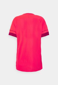 Camiseta atlética de manga corta en rosa brillante, con una textura suave y puños y cuello en contraste de púrpura oscuro.