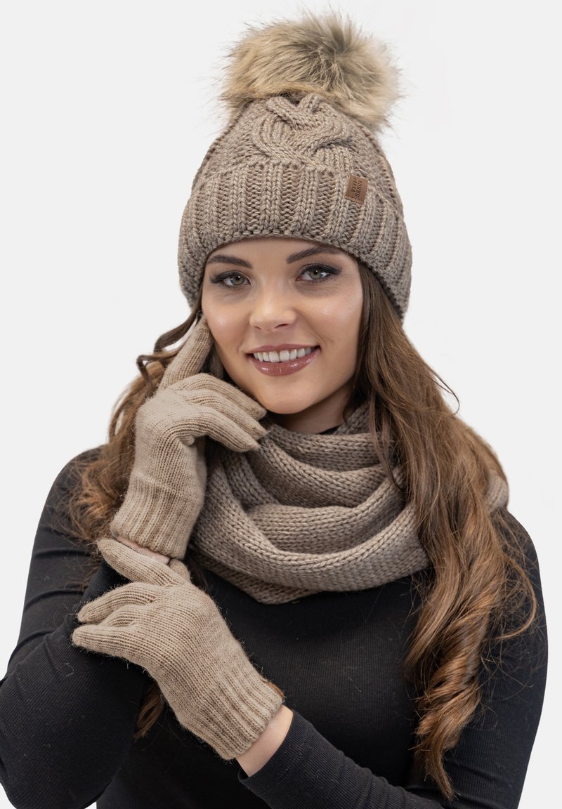 Caciula tricotată maro cu un pom-pom din blană sintetică, mănuși asortate și o eșarfă texturată. Material cald și confortabil cu detalii cu nervuri.