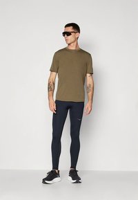 Olivengrønn t-skjorte, marineblå leggings og svarte treningssko. T-skjorten har korte ermer; leggingsene er tettsittende og glatt i teksturen.