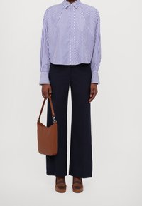 Randig skjorta med knappar i vitt och marinblått, marinblå vida byxor, brun läderväska över axeln och bruna skor med cut-out-detaljer.