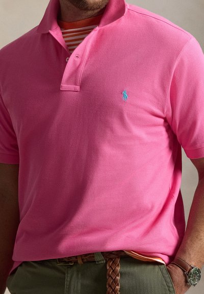 Κοντομάνικο πόλο πουκάμισο σε φωτεινό ροζ βαμβάκι, με μπλε κεντημένο λογότυπο, ριμπ γιακά και διπλό στρώμα με ριγέ λεπτομέρειες.