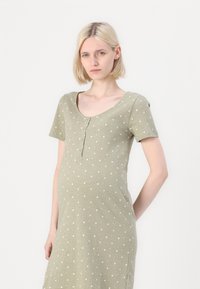 Gaiši zaļš kokvilnas kleita ar īsām piedurknēm, apaļu kakla izgriezumu un baltu zvaigžņu rakstu. Iekļauj pogu plāksni priekšpusē un brīvu piegriezumu.