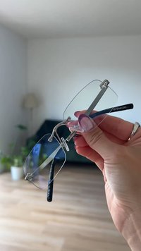 Zilveren metalen montuur brillenglazen met heldere lenzen, ronde vorm en zwarte pootjes met het "even&odd" logo. Vastgehouden tegen een lichte achtergrond.