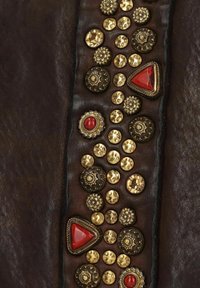 Braunes Lederpanel mit verschiedenen metallischen Nieten in Gold und Schwarz sowie roten geometrischen Steinen, die in einem dekorativen Muster angeordnet sind.