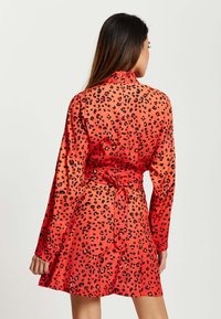 Red dress featuring a black leopard print, long sleeves, high collar, tie waist, and smooth, shiny fabric.