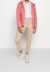 Chaqueta acolchada rosa con capucha, camiseta blanca a rayas, pantalones beige ajustados, y zapatillas blancas, con un acabado texturizado y costuras visibles.