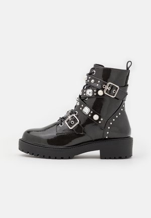 Bottines en cuir verni noir avec plusieurs sangles ornées de boucles argentées et de clous décoratifs, semelle à relief texturé et languette à tirage.