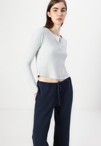 Lichtgrijze geribbelde longsleeve top met een ronde halslijn en knoopdetails, gecombineerd met marineblauwe broek met trekkoord in een losse pasvorm.